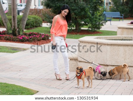 A young woman walking three dogs of pug breed.