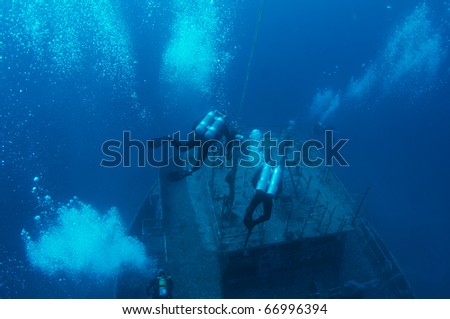 Scuba divers descending upon an artificial reef(a small ship purposely sunk). This artificial reef named the \