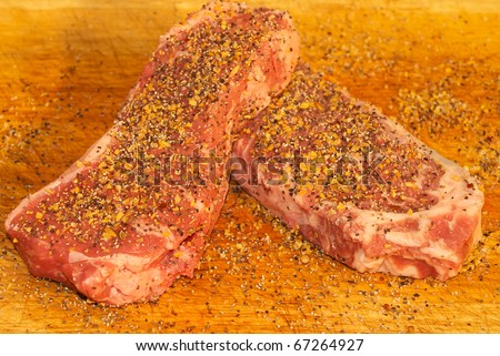 New York Cut Strip Steak on a breadboard, seasoned for the grill.