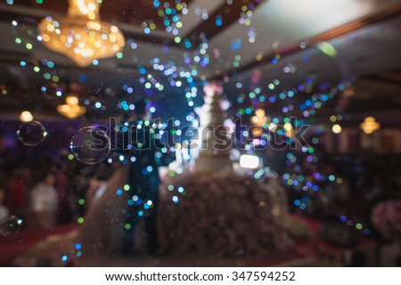 blurred image of cake wedding reception in wedding event party and  beautiful lights decoration inside large hall with people