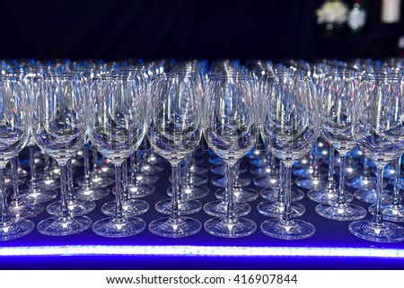a lot of line empty clean wine glasses on a dark background in Blue light at night club
