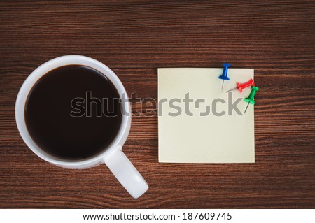 Cup of coffee, sticker and drawing pins on the office desk