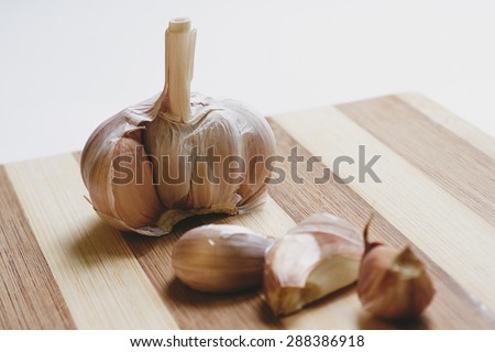 Vertical photo of part of garlic head and three garlic cloves on wooden cutting board