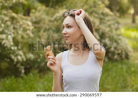 Photo of girl, eating ice-cream in sunglasses and white t-shirt on green blured background