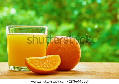Orange, glass with orange juice and orange lobule on the wooden table on green blured background