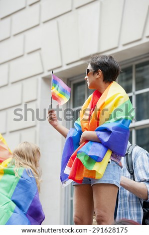 London, UK. 27th June 2015. Revellers enjoy the 2015 Pride In London parade. Young woman watches the parade wrapped in the gay rainbow flag.