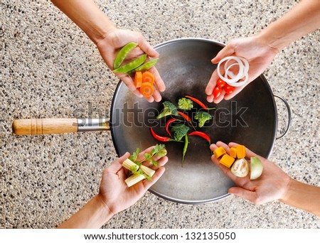 Four hands puts fresh vegetables in the wok. Cooking concept.