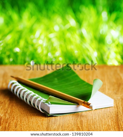 Notepad with cover of leaf lies on wooden board.