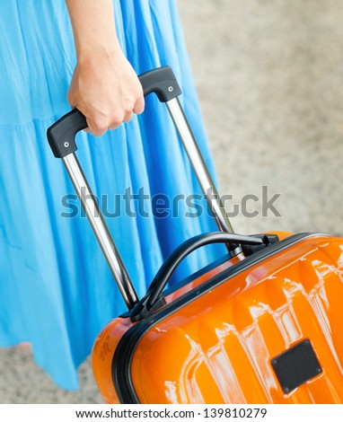Woman in blue dress holds orange suitcase in hand.