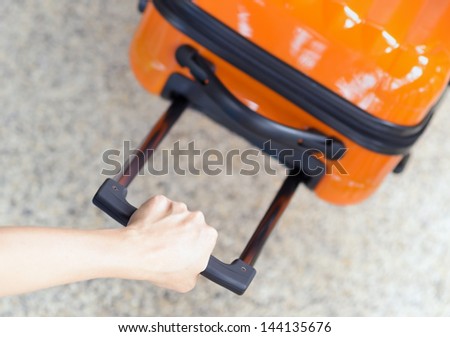 Woman holds orange suitcase in hand.