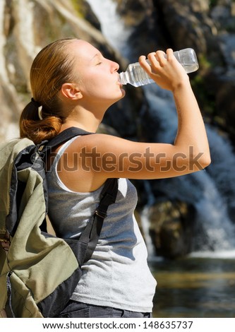Young woman drinks water by waterfall.