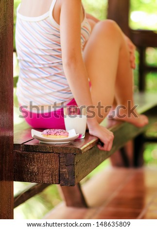 Young woman sitting on terrace with milk and donut.