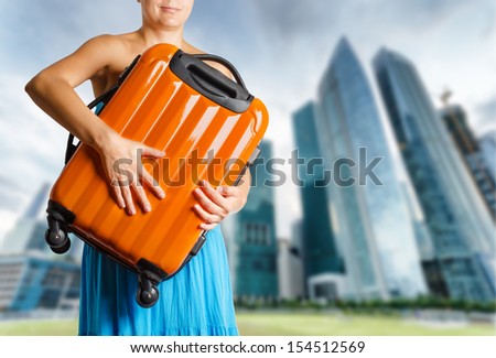 Woman in blue dress holds orange suitcase in hands.