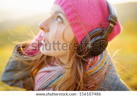 Young woman enjoying a music in the fall season. Autumn outdoor portrait.