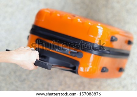 Woman holds orange suitcase in hand.