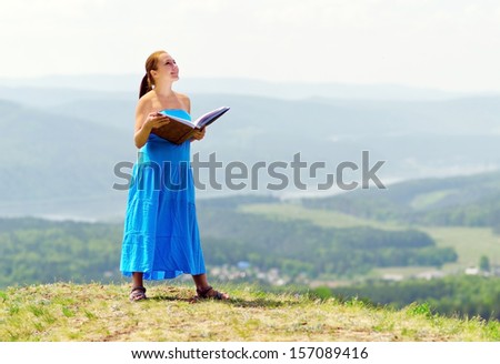 Red haired woman with book on the hilltop.