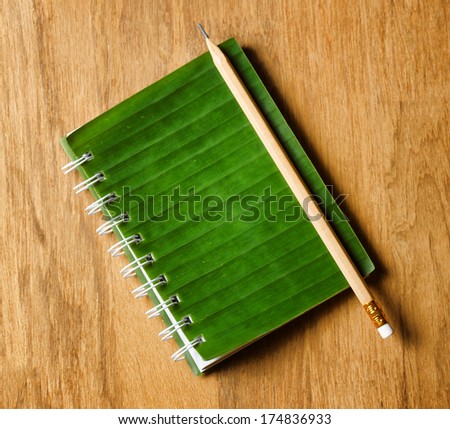 Notepad with cover of leaf lies on wooden board.