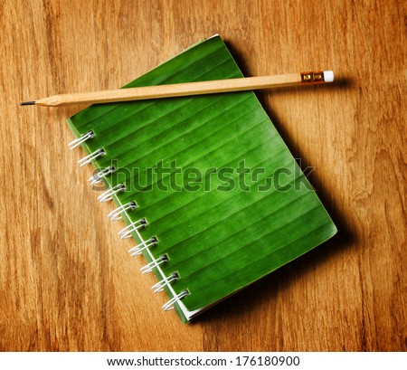 Notepad with cover of leaf lies on wooden board.