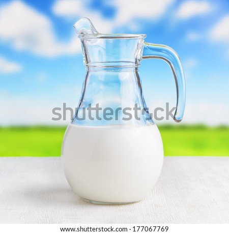 Jug of milk on meadow background. Half full pitcher.