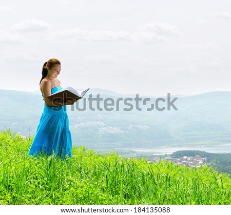 Red haired woman with book on the hilltop.