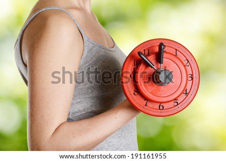Beginner female athlete holding dumbbell with clock dial. Time for fitness.