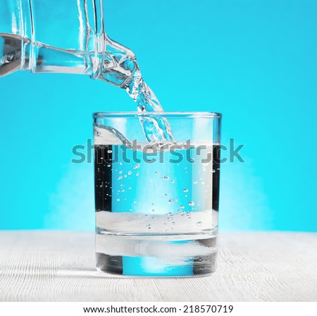 Water pouring into a glass on blue background.