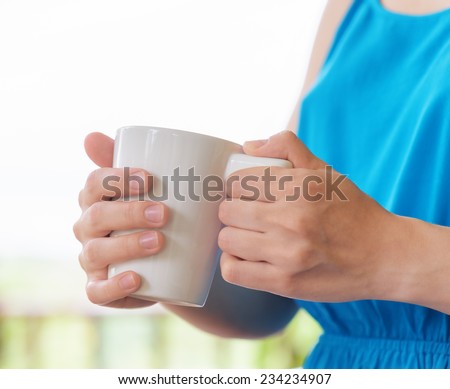 Young woman in blue dress enjoying a mug of beverage. Outdoor portrait. Coffee and tea drinking conception.