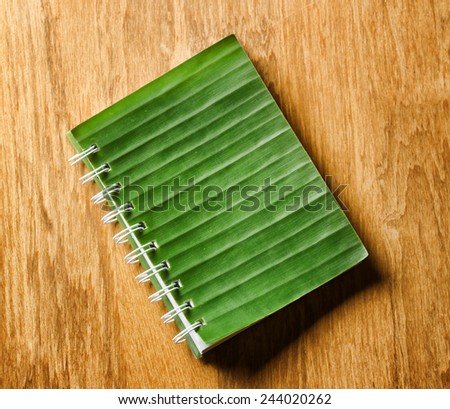 Notepad with cover of leaf lies on wooden board.