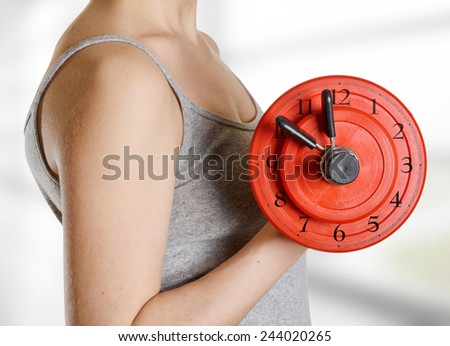 Beginner female athlete holding dumbbell with clock dial. Time for fitness.