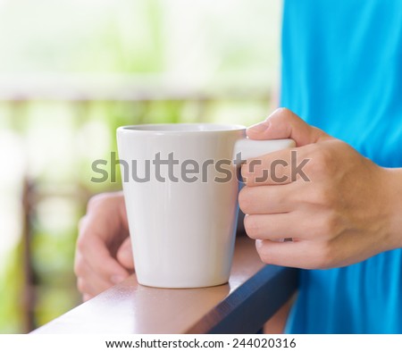 Young woman in blue dress enjoying a mug of beverage. Outdoor portrait. Coffee and tea drinking conception.