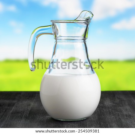 Jug of organic milk on meadow background. Half full pitcher. Eco food rich in calcium and vitamins.