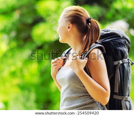 Young smiling woman with backpack in a wood. Hair in a bun. Woman wearing grey clothing. Hiking with camping at summer.