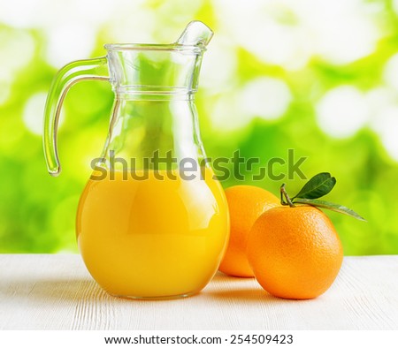 Jug of orange juice and oranges on nature background. Eco food rich in minerals and vitamins. Product of organic farming.