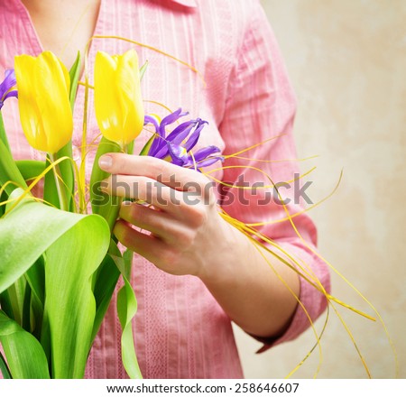 Young woman holding a bouquet of flower and enjoying the beauty and fragrance of yellow tulips and purple irises, creating a spring mood. Woman in fashionable pink blouse.