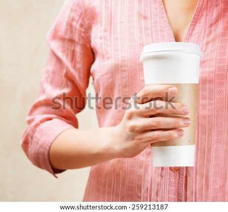 Young woman holding a tumbler of coffee in cafe, drinking and enjoying the aroma of coffee. Woman in fashionable pink blouse.