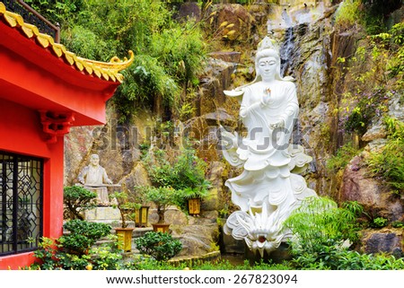 Red roof in Chinese-style and a white Buddhist statue on background of small waterfall in a garden of the Ten Thousand Buddhas Monastery in Hong Kong. Hong Kong is popular tourist destination of Asia.