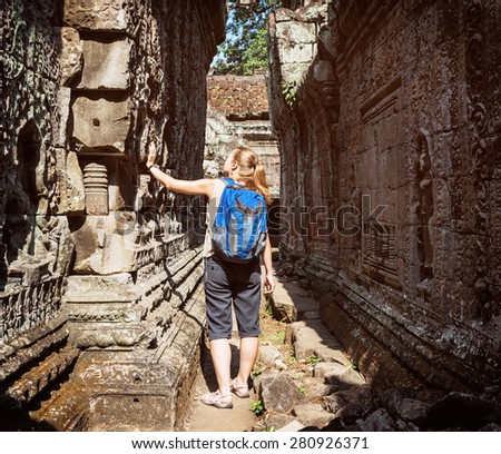Young female tourist with blue backpack looking at the bas-reliefs on the walls of ancient Preah Khan temple in Angkor. Siem Reap, Cambodia.