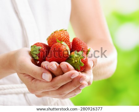 Closeup view of fresh ripe red strawberries in hands of young woman in white dress on nature background. Healthy eco sweet food rich in vitamins. Product of organic farming.