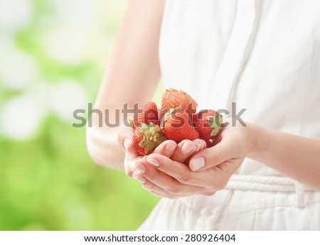 Handful of fresh ripe juicy strawberries in hands of young woman in white dress on nature background. Healthy eco sweet food rich in vitamins. Popular product of organic farming.