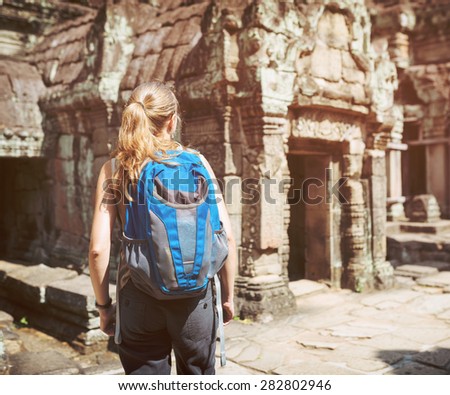 Young female tourist with blue backpack walking among mysterious ruins of ancient Preah Khan temple in Angkor. Siem Reap, Cambodia. Toned image.