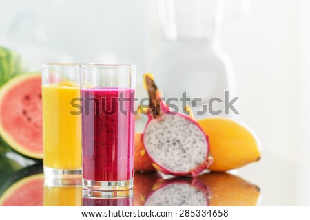 Fresh fruit smoothies on kitchen table. Blender is visible in background. Yellow mango juice and red pitaya juice on fruits background. Healthy eco food rich in vitamins.