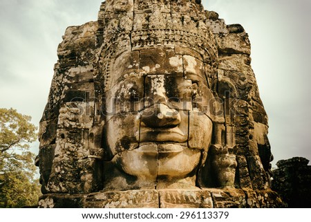 Enigmatic smiling giant stone face of ancient Bayon temple in Angkor Thom, Siem Reap, Cambodia. Mysterious Angkor Thom nestled among rainforest. It is a popular tourist attraction. Toned image.