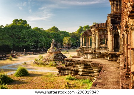 Buddhist Stupa and outer hallway with columns of ancient temple complex Angkor Wat in Siem Reap, Cambodia. Blue sky and woods in background. Mysterious Angkor Wat is a popular tourist attraction.