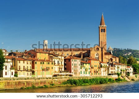 Beautiful view of colorful facades of old houses on waterfront of the Adige River in Verona, Italy. The Santa Anastasia church on blue sky background. Verona is a popular tourist destination of Europe