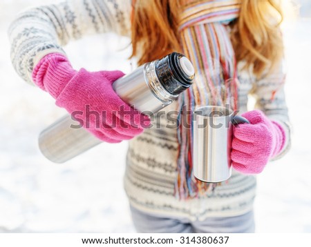 Woman pouring a hot drink in mug from thermos.
