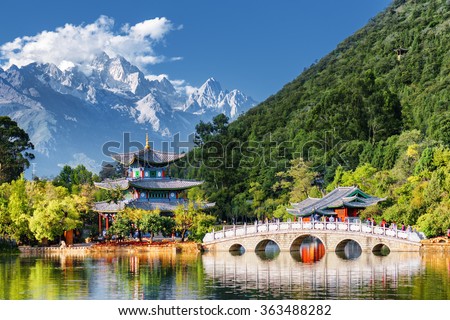 Amazing view of the Jade Dragon Snow Mountain and the Black Dragon Pool, Lijiang, Yunnan province, China. The Suocui Bridge over pond and the Moon Embracing Pavilion in the Jade Spring Park.