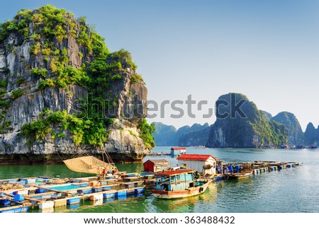 Floating fishing village in the Halong Bay (Descending Dragon) at the Gulf of Tonkin of the South China Sea, Vietnam. Landscape formed by karst towers-isles in various sizes. Blue sky in background.