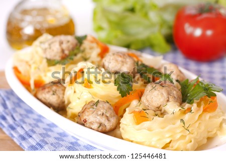 Tagliatelle with meatballs on a white plate, red tomatoes, green salad and olive oil in background