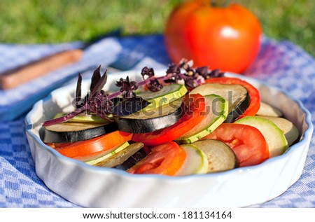 Sliced tomatoes, eggplant and zucchini in a round dish for ratatouille on a green background