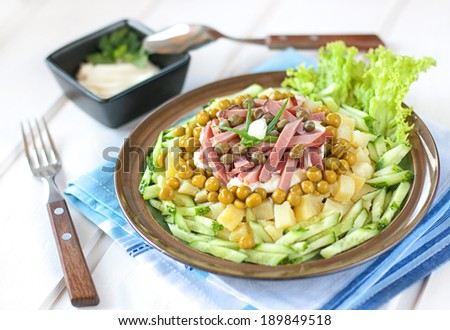 Polish salad with potatoes, ham, cucumber, green peas, capers and mayonnaise on a round plate